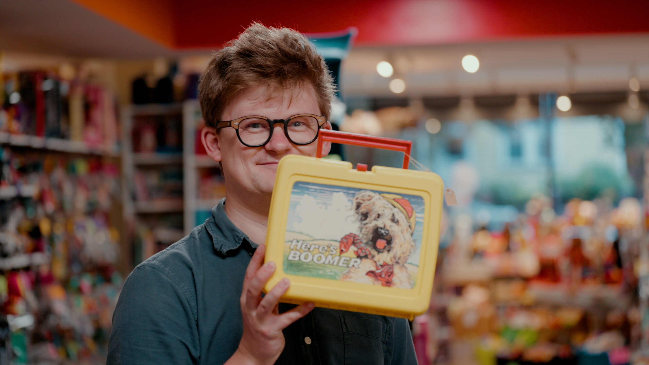 Tom Nicholas holding up a lunch box, which has a photo of a dog and the words "Here's Boomer" on it.